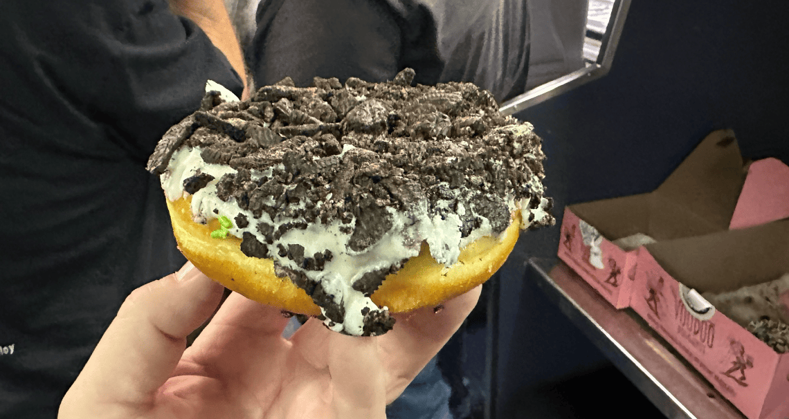 A hand holding a donut with a chocolate topping

Description automatically generated