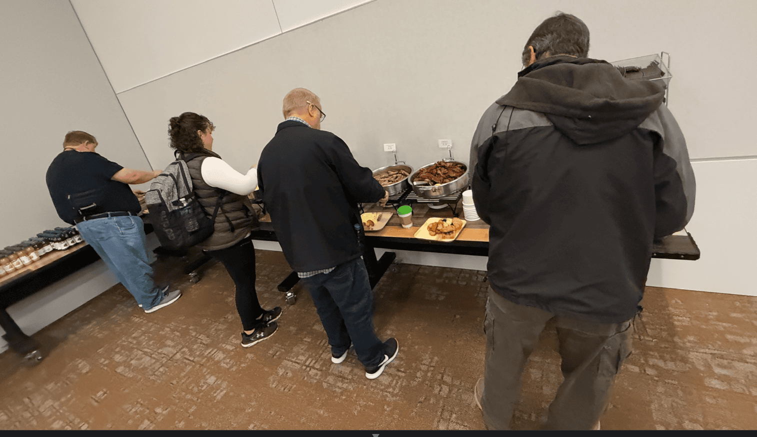 A group of people standing in front of a table full of food

Description automatically generated